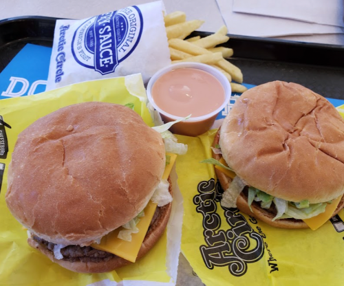 Two burgers with cheese and lettuce, a cup of dipping sauce, and a side of fries on a tray.