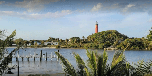 A scenic view of a lighthouse on a lush island, surrounded by water and palm trees under a clear blue sky.