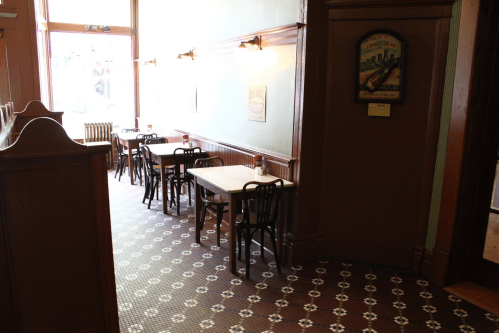A cozy dining area with wooden tables and chairs, featuring patterned tile flooring and soft lighting.