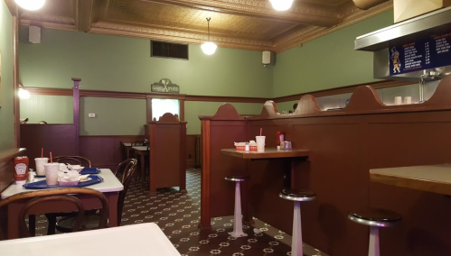 A cozy diner interior with wooden booths, tables, and a checkered floor, featuring ketchup and condiment bottles on tables.