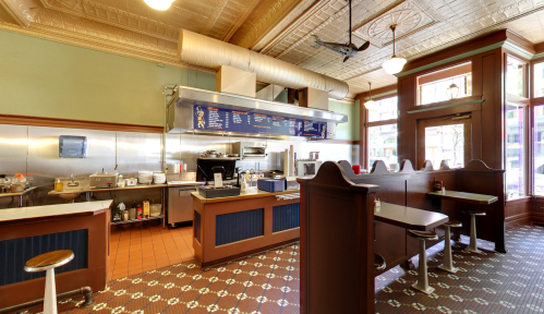 A vintage-style diner interior featuring a kitchen area, booths, and decorative tile flooring.