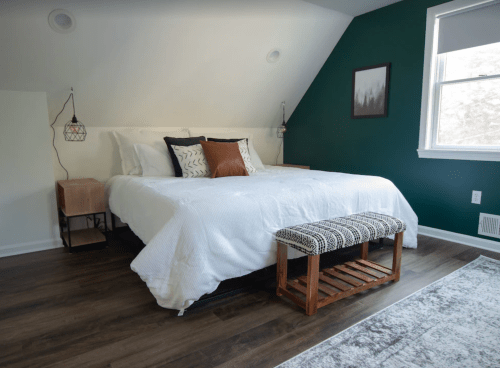 Cozy bedroom with a sloped ceiling, a bed with white bedding, a wooden bench, and green accent wall.