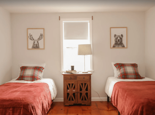Two twin beds with red blankets, framed animal prints on the walls, and a wooden nightstand with a lamp in a bright room.