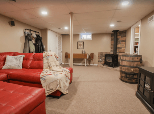 Cozy basement living area with a red sectional sofa, a small desk, and a stone fireplace. Warm and inviting atmosphere.