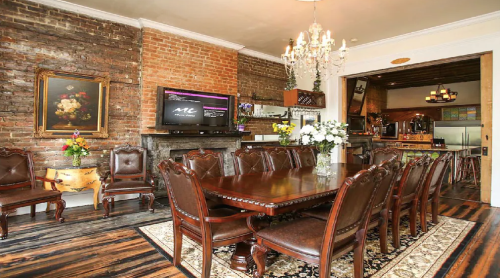 Elegant dining room with a large wooden table, vintage chairs, exposed brick walls, and a chandelier.
