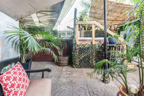 A cozy outdoor space with potted plants, a wooden structure, and a bench with a patterned cushion.