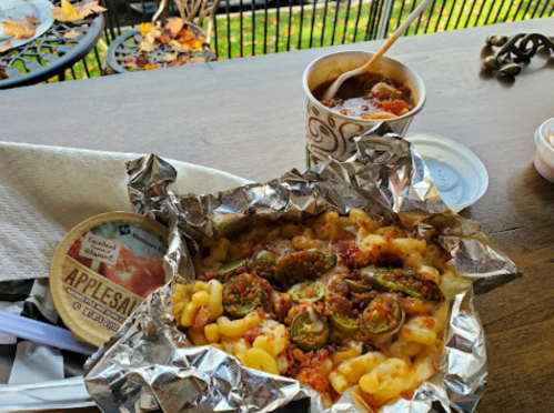 A meal featuring macaroni and cheese with jalapeños, a cup of chili, and a container of applesauce on a table.