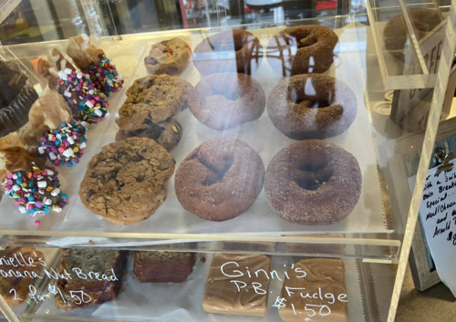 A display case filled with various baked goods, including cookies and chocolate donuts, with prices listed.
