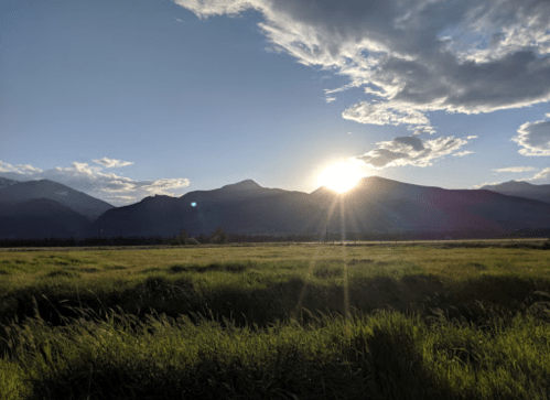 Sunset over mountains with a grassy foreground, casting a warm glow and creating a serene landscape.
