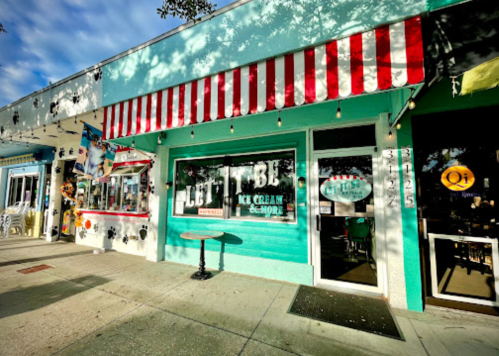 A colorful ice cream shop with a striped awning and outdoor seating, surrounded by other storefronts.