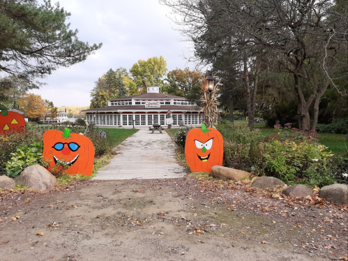 A pathway lined with cartoonish pumpkin decorations leads to a large building surrounded by trees and autumn foliage.