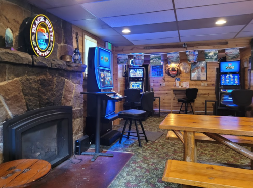 Cozy interior of a gaming room with slot machines, a fireplace, and wooden tables in a rustic setting.