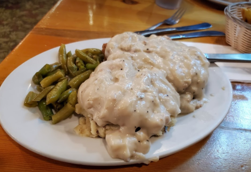 A plate of biscuits smothered in creamy gravy, served with a side of green beans.
