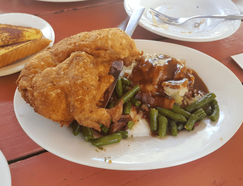 A plate of fried chicken with green beans, mashed potatoes, and gravy, alongside a piece of French toast.