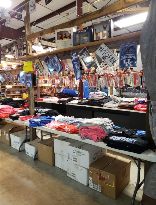 A display of folded t-shirts in various colors on tables, surrounded by sports memorabilia and merchandise.