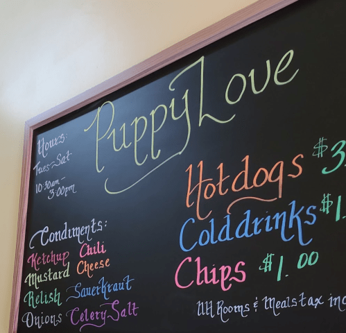 Chalkboard menu for "Puppy Love" listing hours, hotdogs, cold drinks, chips, and various condiments.