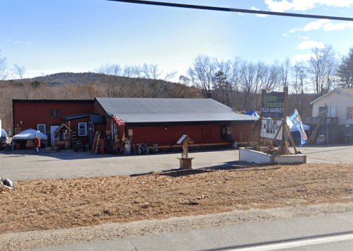 A red building with a black roof, featuring a flea market sign and outdoor displays, set against a mountainous backdrop.