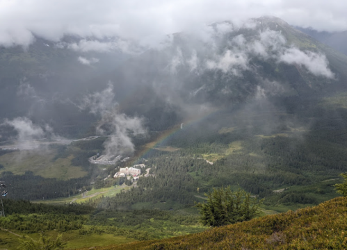 A scenic view of a valley with a small village, surrounded by mountains and misty clouds.