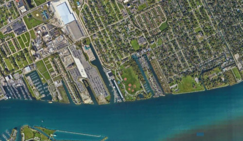 Aerial view of a waterfront area featuring parks, buildings, and a marina along a blue river or lake.