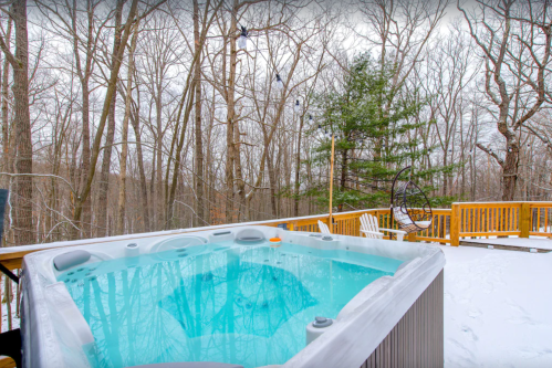 A hot tub on a snowy deck surrounded by bare trees, creating a serene winter landscape.