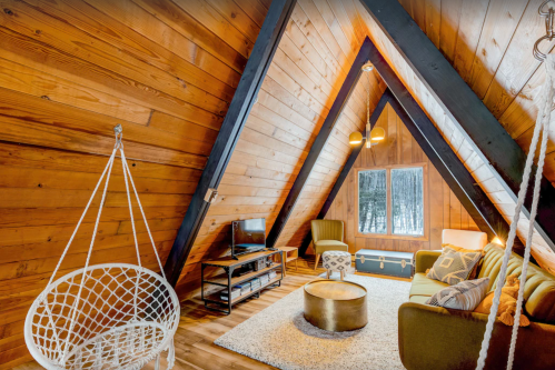 Cozy A-frame living room with wooden walls, a hanging chair, and modern furniture, featuring a warm, inviting atmosphere.