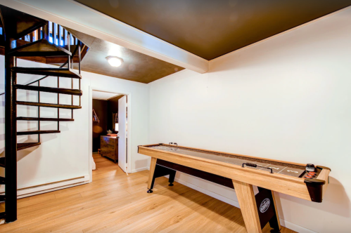 A spacious room featuring a shuffleboard table and a spiral staircase leading to an upper level.