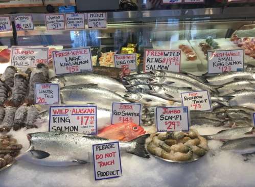 A seafood display featuring various fish, including salmon, red snapper, and shrimp, with price tags on ice.