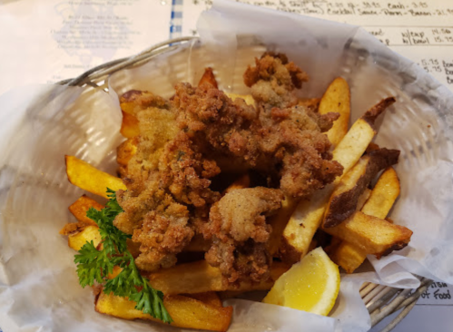 A basket of crispy fried chicken pieces on a bed of golden fries, garnished with a lemon wedge and parsley.