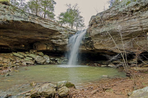 A serene waterfall cascades into a tranquil pool surrounded by rocky terrain and lush greenery.