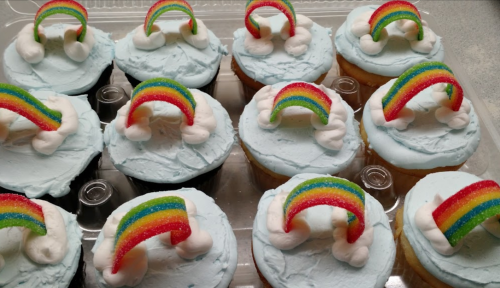 A tray of cupcakes with blue frosting, topped with marshmallow clouds and rainbow candy decorations.