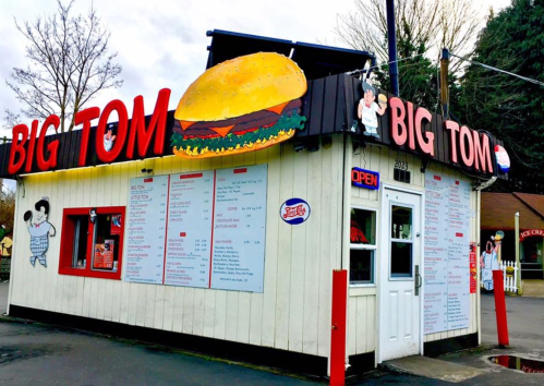 A small fast-food stand named "Big Tom" with a large burger sign and a menu displayed outside.