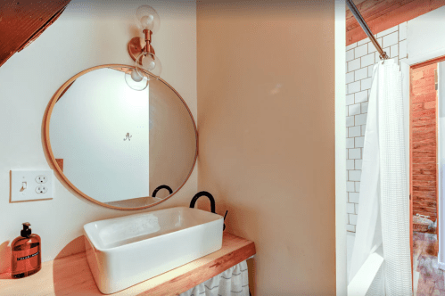 A modern bathroom featuring a round mirror, a white sink on a wooden countertop, and a shower area with a curtain.