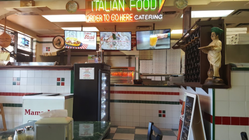 Interior of an Italian restaurant featuring a menu board, display cases, and a statue, with a neon sign overhead.