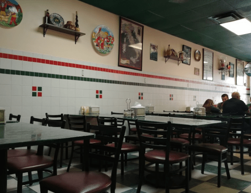 Interior of a casual restaurant with green and red decor, empty tables, and a few patrons in the background.