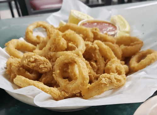 A plate of golden-brown fried calamari rings served with lemon wedges and marinara sauce.