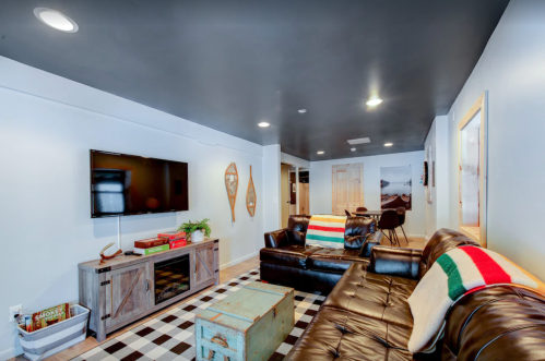 Cozy living room with a dark ceiling, leather sofa, TV, and decorative accents on a checkered floor.