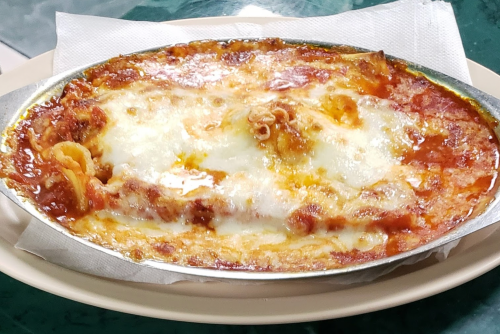 A baked lasagna dish with layers of pasta, meat, and melted cheese, served in a metal tray on a plate.