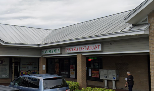 Exterior of a pizzeria restaurant named "Mamma Mia" with a metal roof and nearby mailboxes.