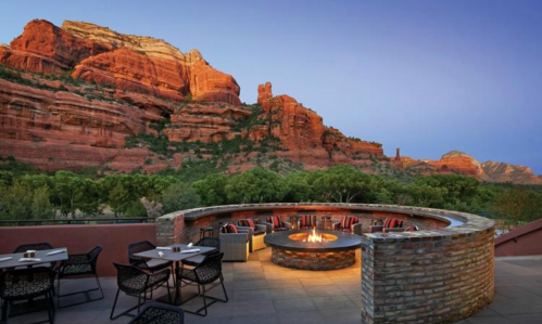 A scenic outdoor patio with a fire pit, surrounded by red rock formations and trees at dusk.