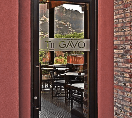 View through a glass door of a restaurant named "Ti Gavo," showcasing a cozy interior and outdoor seating.