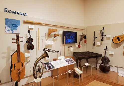 Display of traditional Romanian musical instruments, including violins, flutes, and a cimbalom, in a museum setting.