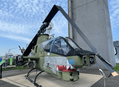 A military helicopter with a shark mouth design displayed outdoors, set against a cloudy sky.