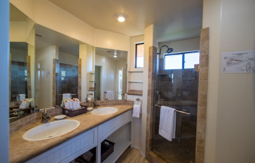 Spacious bathroom with double sinks, a walk-in shower, and large mirrors, featuring neutral tones and natural light.