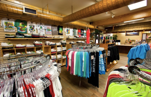 A retail store interior showcasing colorful clothing on racks and shelves, with a tropical theme decor.