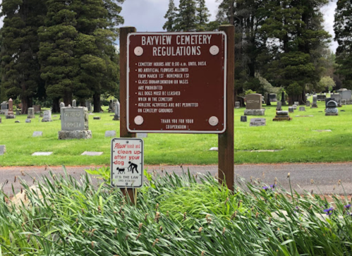 Signage at Bayview Cemetery outlining regulations, with a notice about cleaning up after dogs in the foreground.