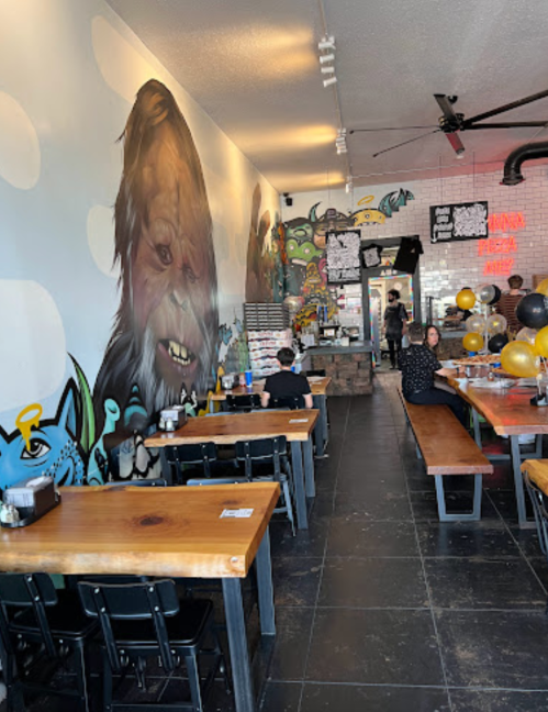 A vibrant restaurant interior with mural art, long wooden tables, and balloons, featuring a character on the wall.