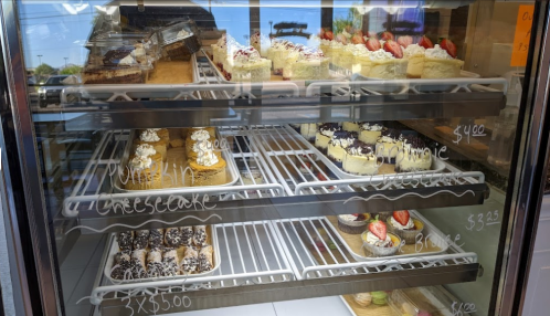 A display case filled with various cakes and cheesecakes, including chocolate and strawberry options.