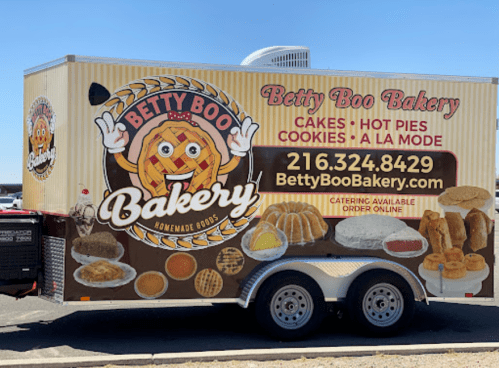 A food truck for Betty Boo Bakery featuring cakes, hot pies, and cookies, with contact information displayed.