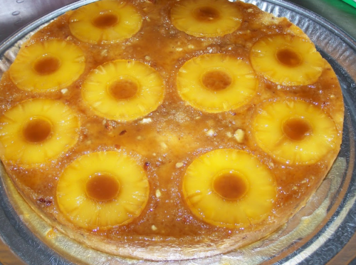 A round pineapple upside-down cake topped with caramelized pineapple rings on a silver platter.