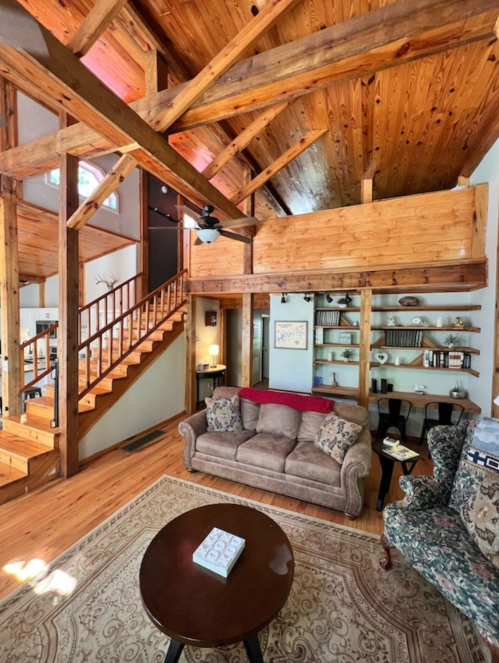 Cozy living room with wooden beams, a staircase, and a mix of comfortable furniture and bookshelves.